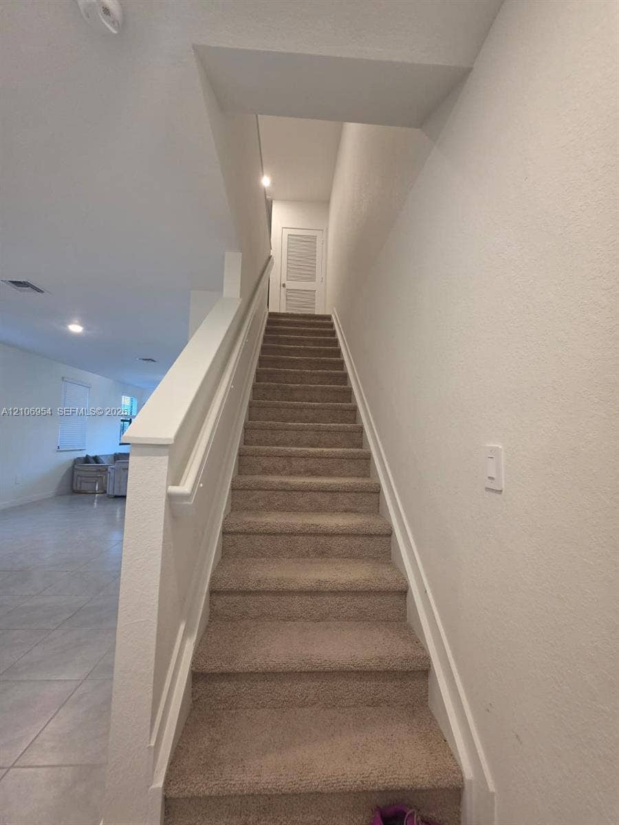 Staircase featuring wall-to-wall carpeting, painted wooden handrails, and louvered door access