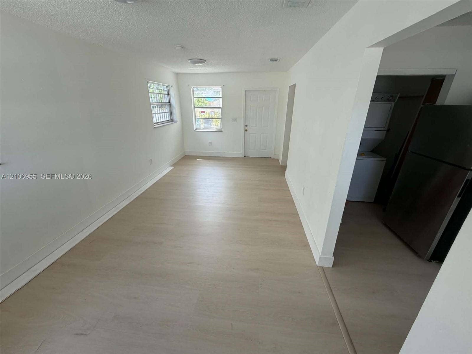 Interior space featuring light wood-finish flooring, neutral wall tones, multi-pane windows, and a dedicated laundry area with stacked appliances
