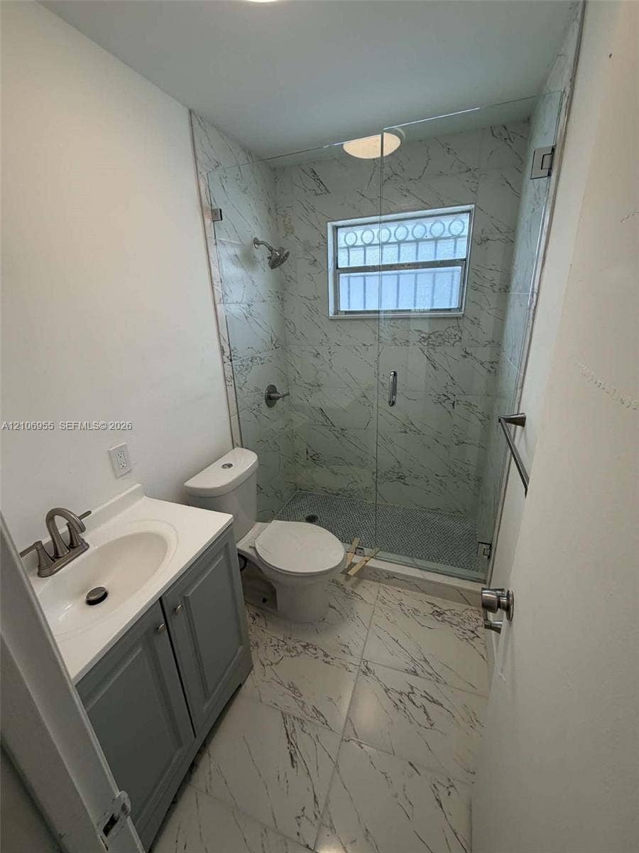 Bathroom featuring stone-finish wall and floor tiling, walk-in shower with a glass enclosure, grey cabinetry with a white countertop, and integrated sink