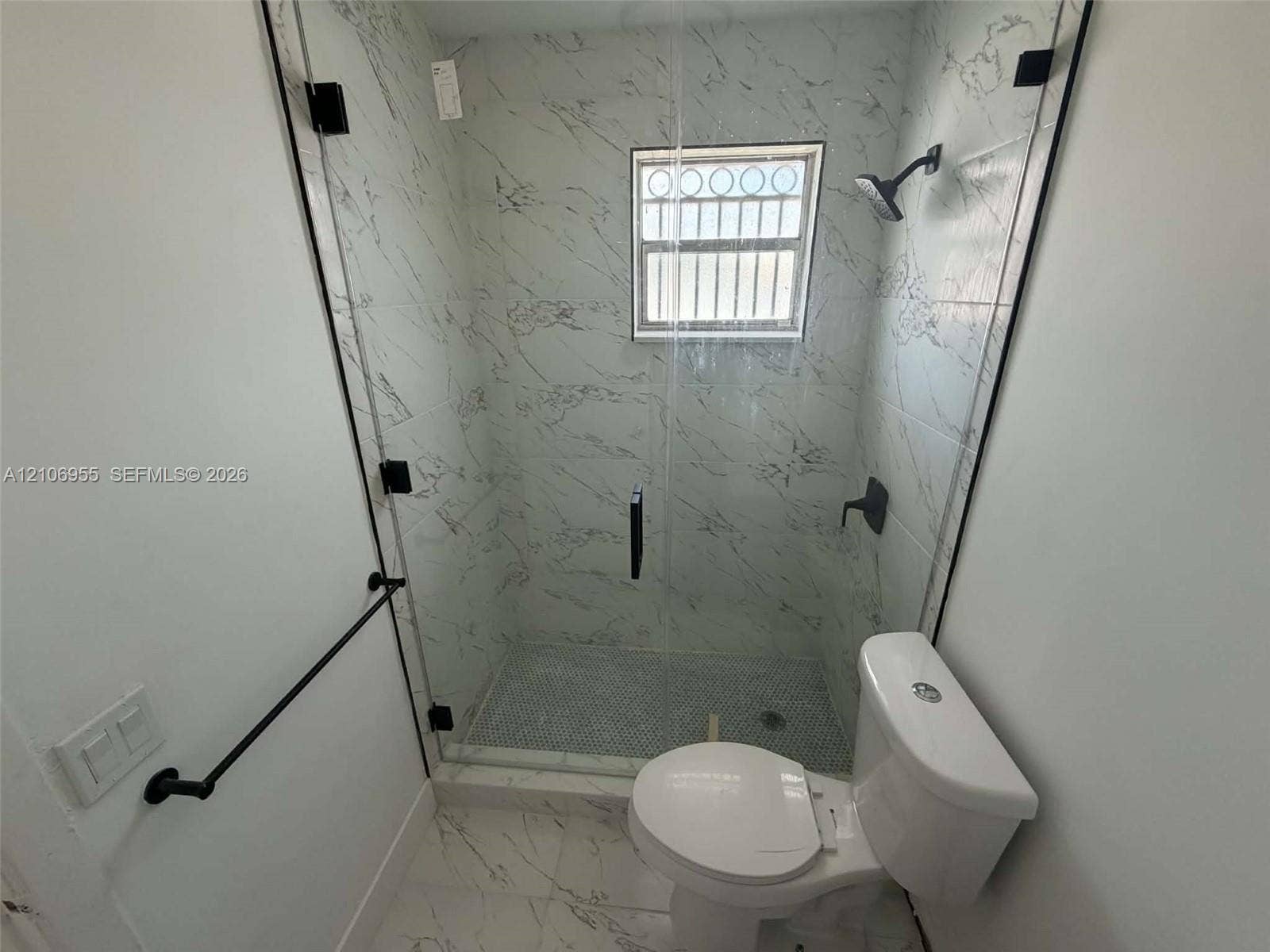 Walk-in shower featuring glass enclosure, stone-finish wall tile, penny tile flooring, and matte black hardware