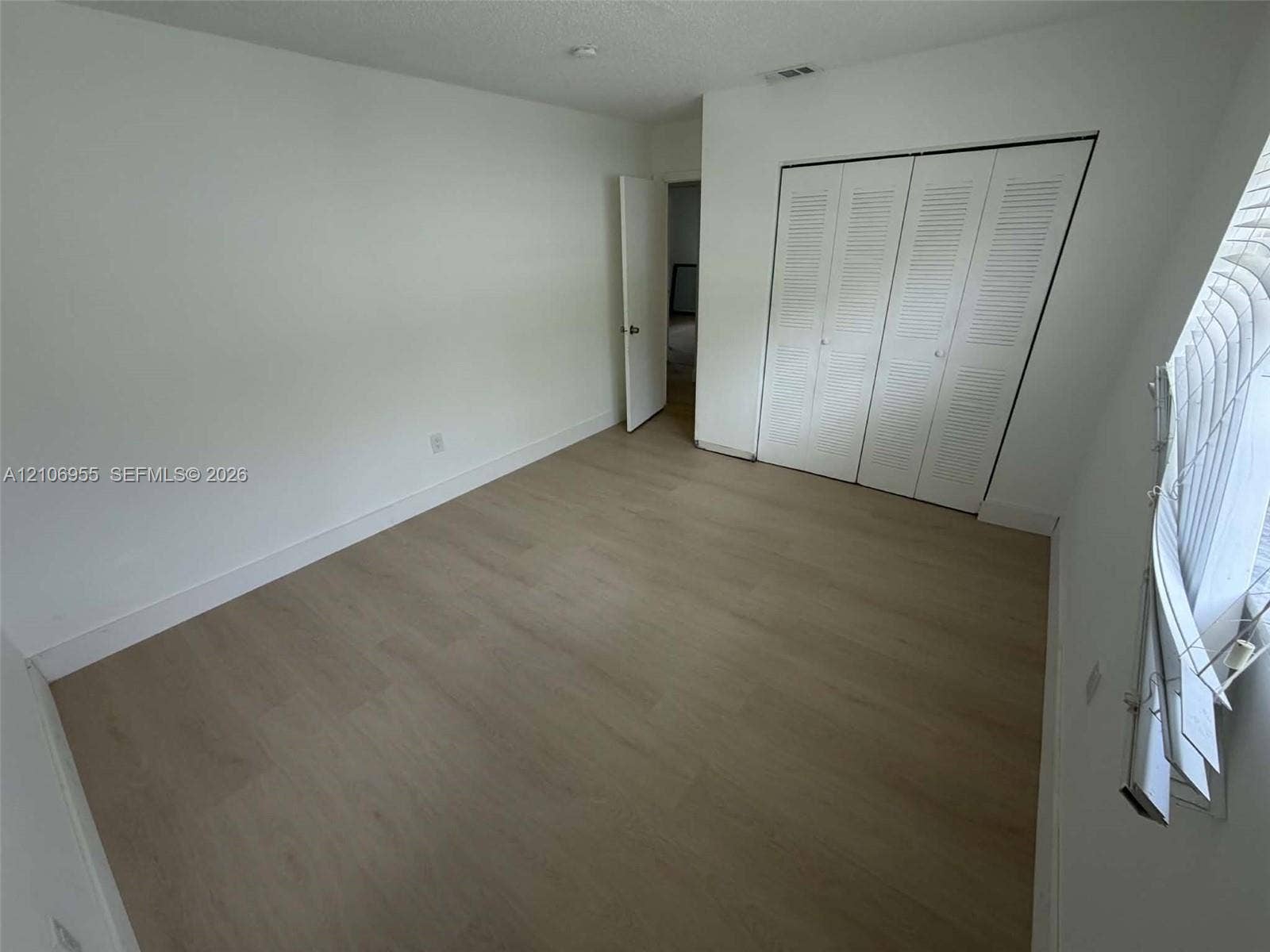 Room featuring wood-finish flooring, white walls, and a bi-fold louvered closet door
