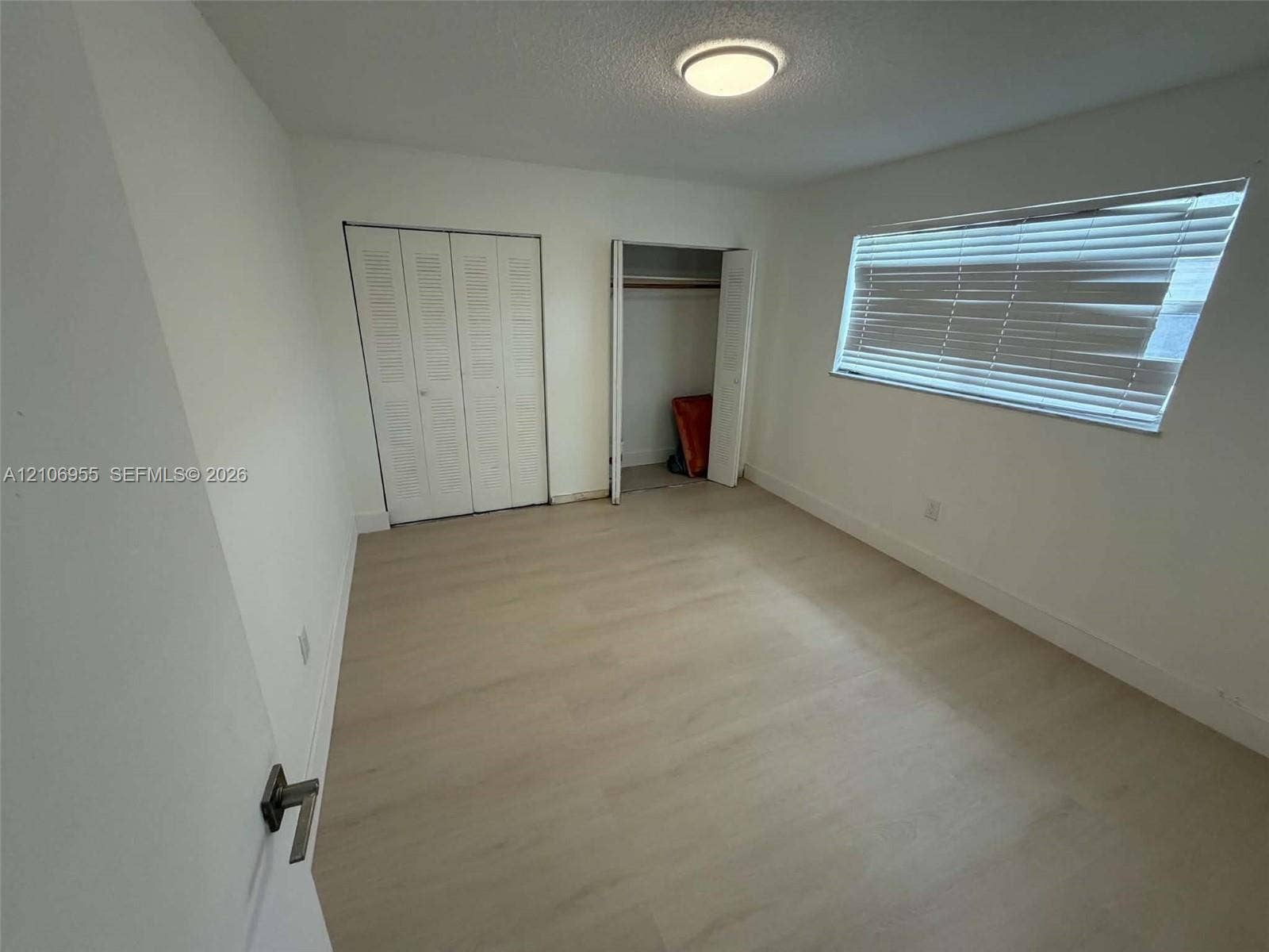 Interior room featuring wood-finish flooring, two closets with louvered doors, and a window with horizontal blinds