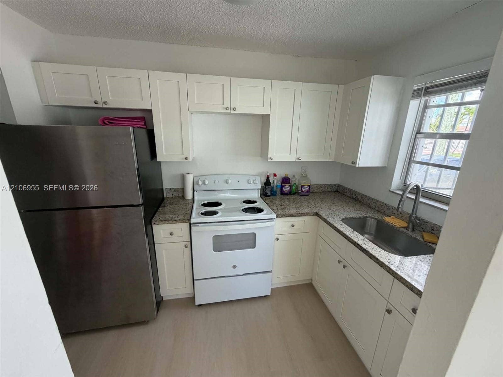 Kitchen featuring white shaker-style cabinetry, stone-finish countertops, stainless steel refrigerator, white electric range, and stainless steel sink with a gooseneck faucet