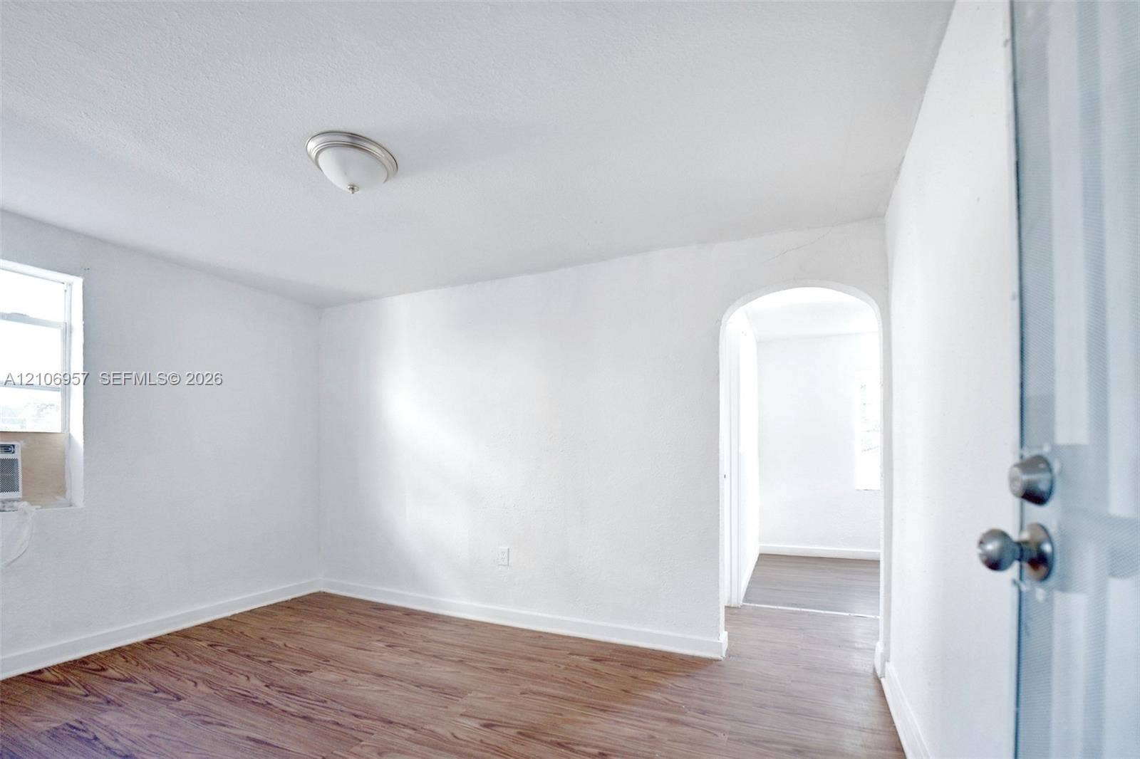 3660 NW 20th Avenue, #4, Miami, Miami, FL 33142 Room featuring wood-finish flooring, white walls, an arched entryway, and a flush-mount ceiling light fixture
