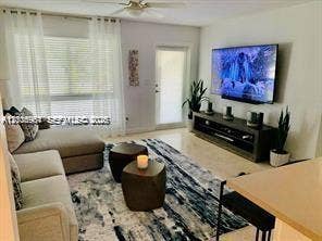 Living area featuring large windows with window treatments, neutral flooring, a ceiling fan, and a glass-paneled exterior door