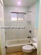 Full bathroom featuring a white porcelain tub, light-toned wall tile surround, shower fixture, and a window