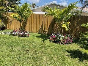 Enclosed backyard featuring a wood privacy fence, mature palm trees, flowering shrubs, and a lawn