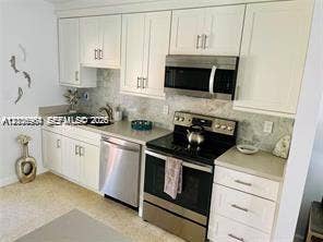 Kitchen featuring white shaker-style cabinetry, neutral stone-finish countertops, tiled backsplash, and stainless steel appliances including a range, microwave, and dishwasher