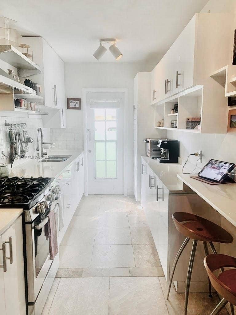 8540 Byron Avenue, #1B, Miami Beach, Miami Beach, FL 33141 Galley kitchen featuring high-gloss white cabinetry, stone-finish countertops, tile flooring, built-in open shelving, and a stainless steel gas range