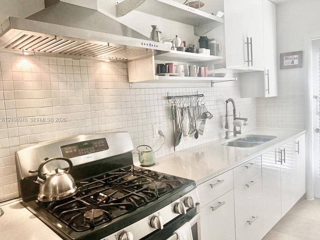 8540 Byron Avenue, #1B, Miami Beach, Miami Beach, FL 33141 Kitchen featuring a stainless steel gas range, professional-grade range hood, white flat-panel cabinetry, white square-tile backsplash, and solid-surface countertops with a double-basin undermount sink