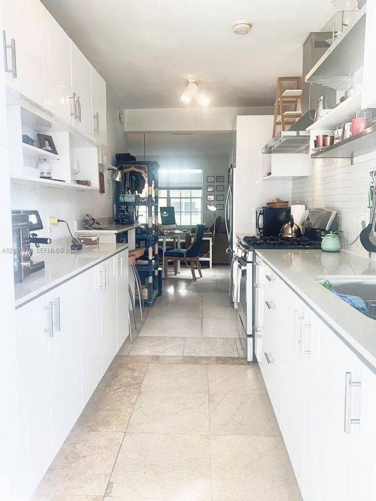 8540 Byron Avenue, #1B, Miami Beach, Miami Beach, FL 33141 Galley kitchen featuring white flat-panel cabinetry, light-toned stone-finish flooring, solid-surface countertops, and a subway-style tile backsplash