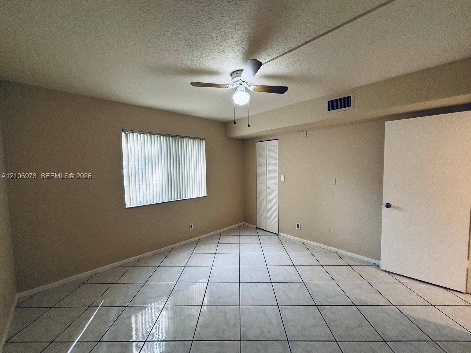 504 Gardens Drive, #101, Pompano Beach, Pompano Beach, FL 33069 Room featuring neutral wall paint, tile flooring, ceiling fan with integrated light fixture, vertical window blinds, and a louvered-panel closet door