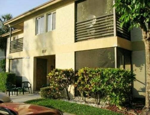 504 Gardens Drive, #101, Pompano Beach, Pompano Beach, FL 33069 Two-story exterior featuring a stucco facade, screened-in porch, upper-level balcony with horizontal slat railings, and manicured shrubbery