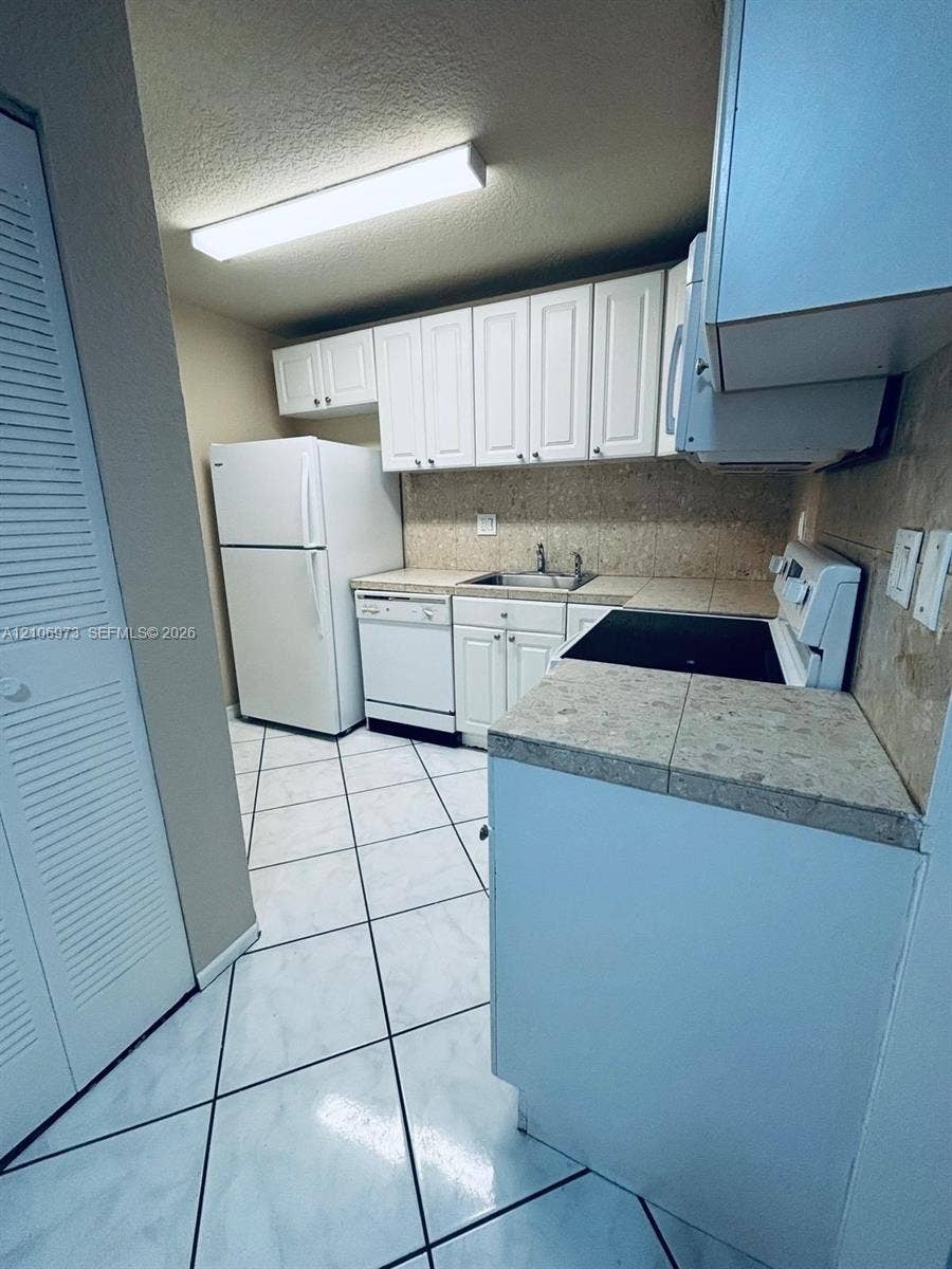 504 Gardens Drive, #101, Pompano Beach, Pompano Beach, FL 33069 Kitchen featuring white cabinetry, tiled countertops, a double-basin stainless steel sink, ceramic tile flooring, and integrated white appliances