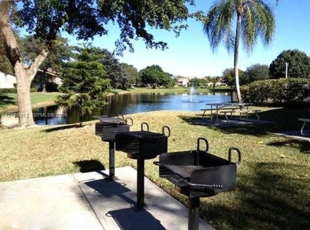 504 Gardens Drive, #101, Pompano Beach, Pompano Beach, FL 33069 Outdoor common area featuring permanent steel charcoal grills, a concrete pad, mature trees, and a water feature with a fountain