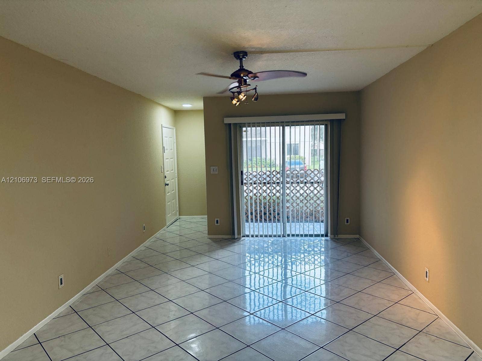 504 Gardens Drive, #101, Pompano Beach, Pompano Beach, FL 33069 Neutral-toned interior featuring large-format tile flooring laid on a diagonal, sliding glass patio door, and a ceiling fan with multi-light fixture