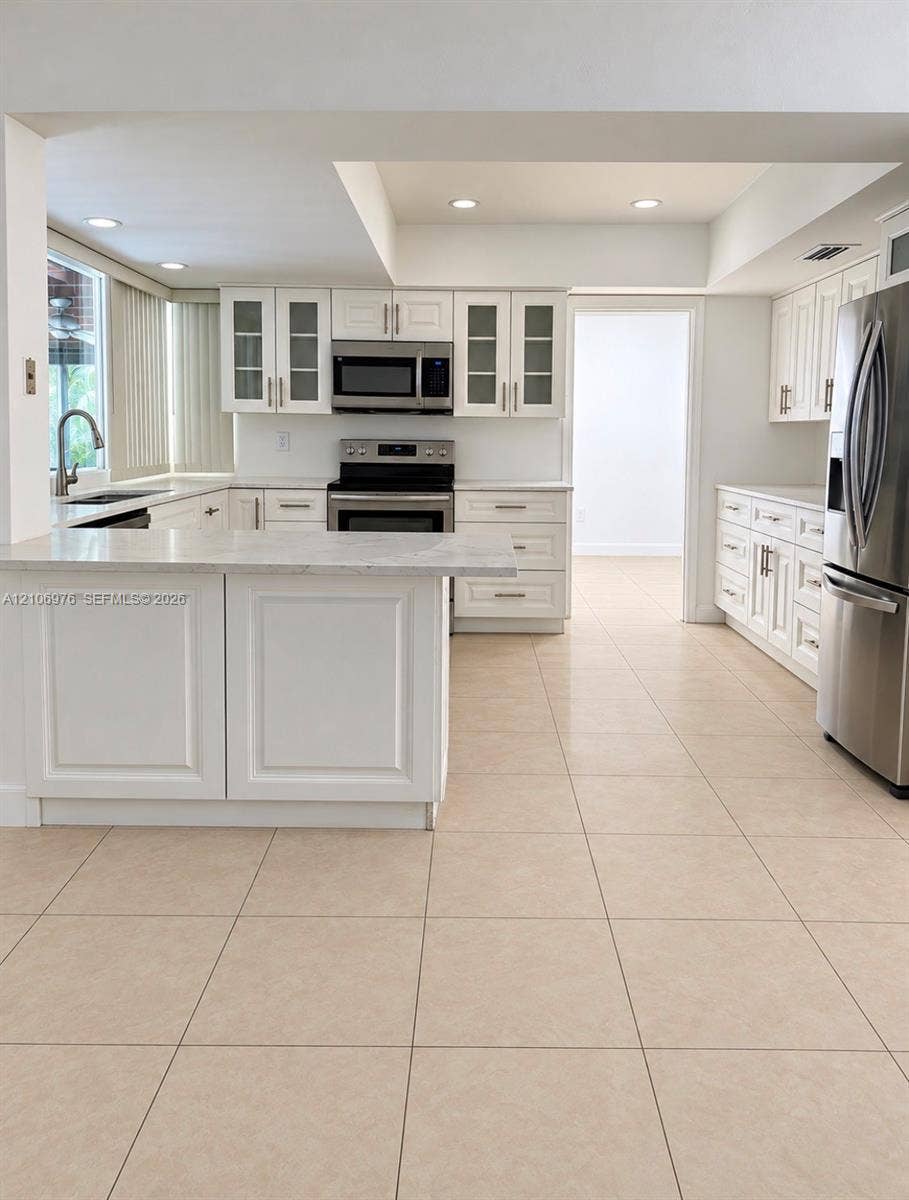 8376 NW 16th Street, Coral Springs, Coral Springs, FL 33071 Kitchen featuring white shaker-style cabinetry, a peninsula with stone-finish countertops, stainless steel appliances, and tile flooring