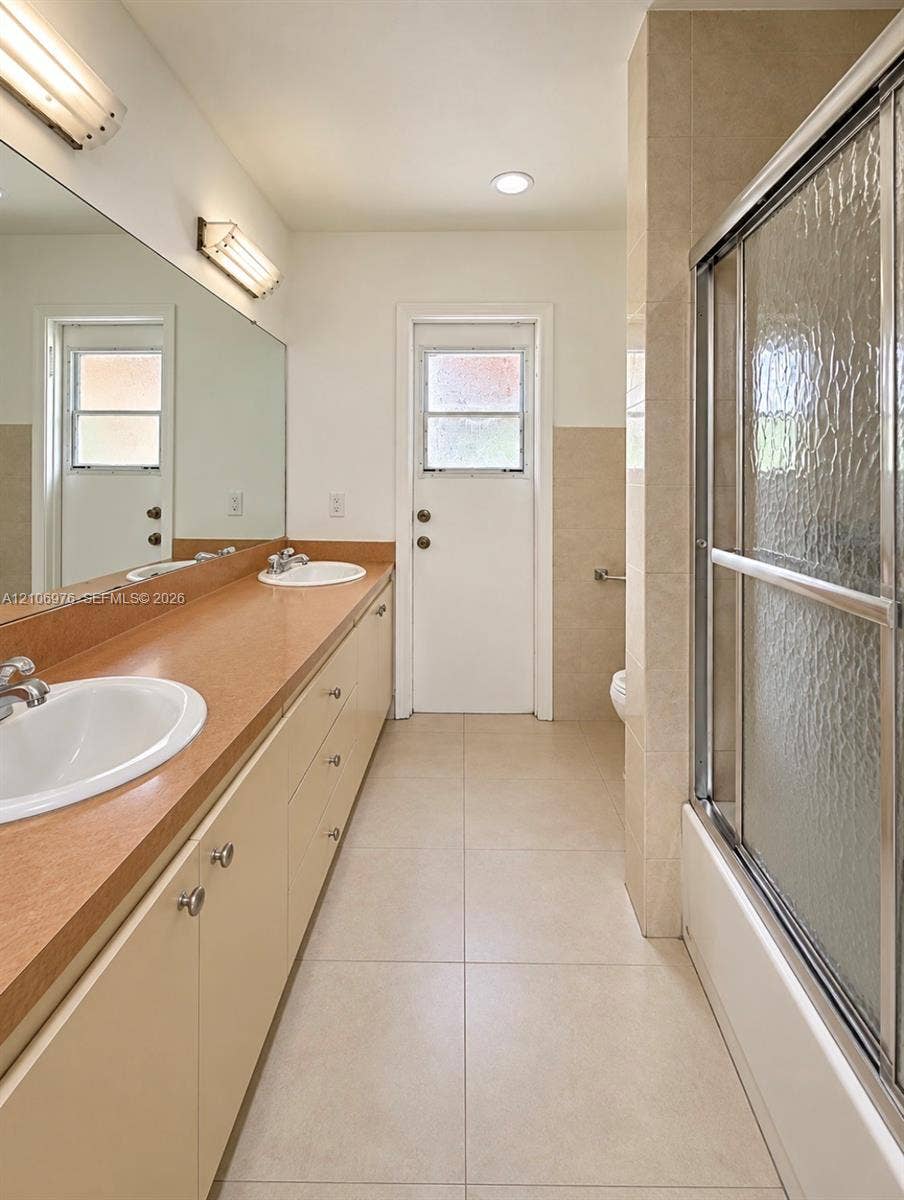 8376 NW 16th Street, Coral Springs, Coral Springs, FL 33071 Extended vanity with dual undermount sinks, solid-surface countertop, full-width wall mirror, and tub-shower combination with sliding textured glass doors