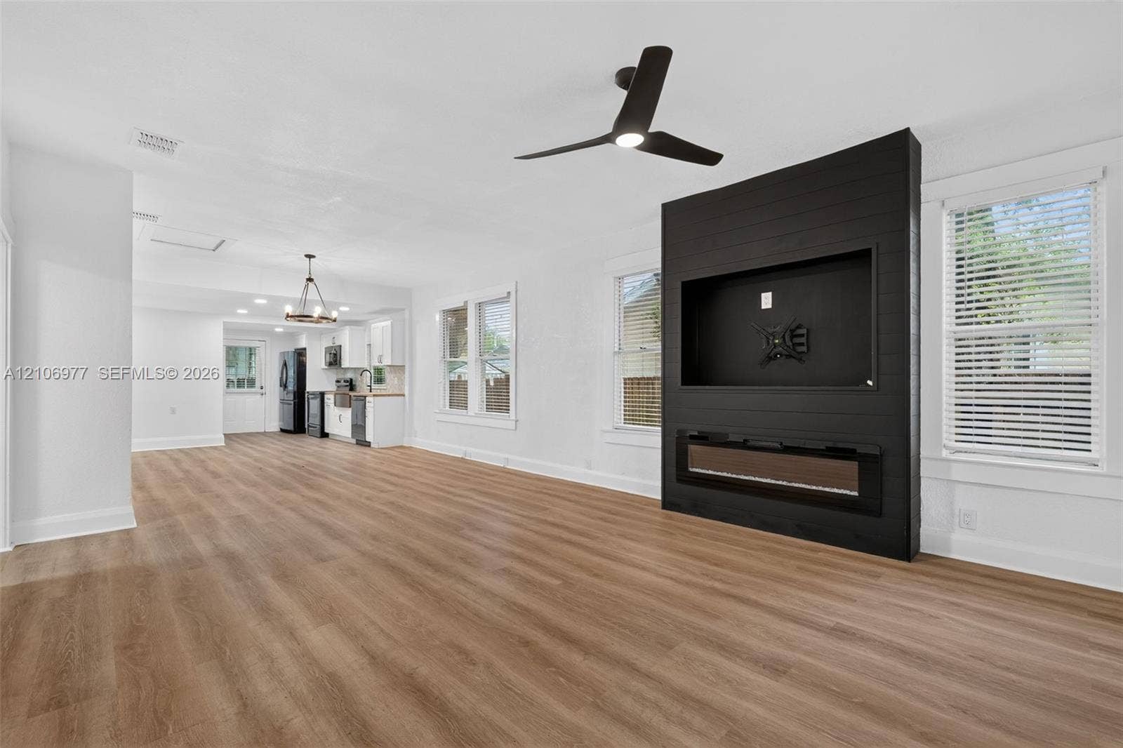 Open-concept space featuring wood-finish flooring, a matte black shiplap accent wall with a built-in electric fireplace, and a three-blade ceiling fan