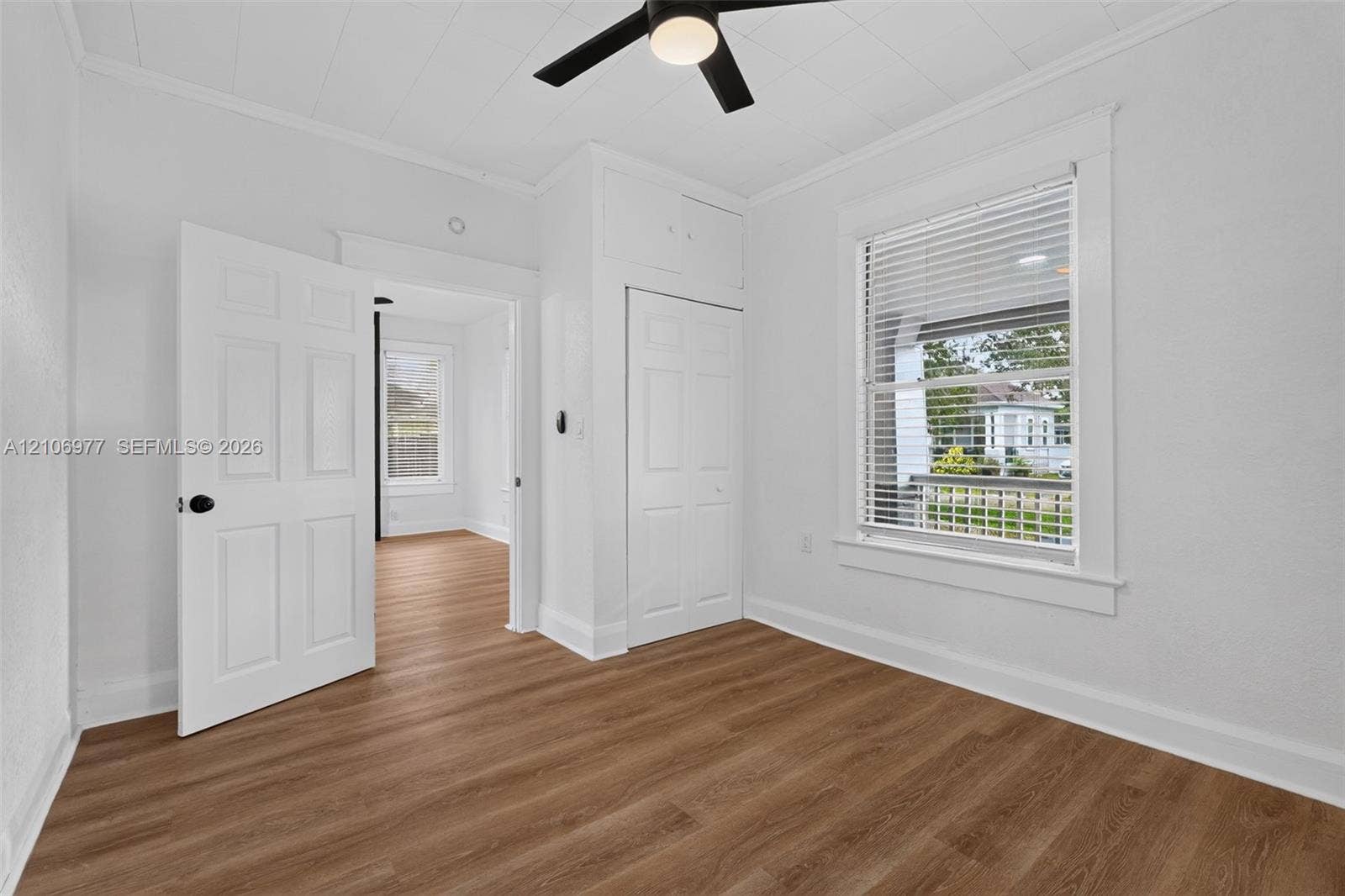 Interior room featuring wood-finish flooring, a ceiling fan with integrated lighting, a single-hung window with wood casing, and built-in closet cabinetry