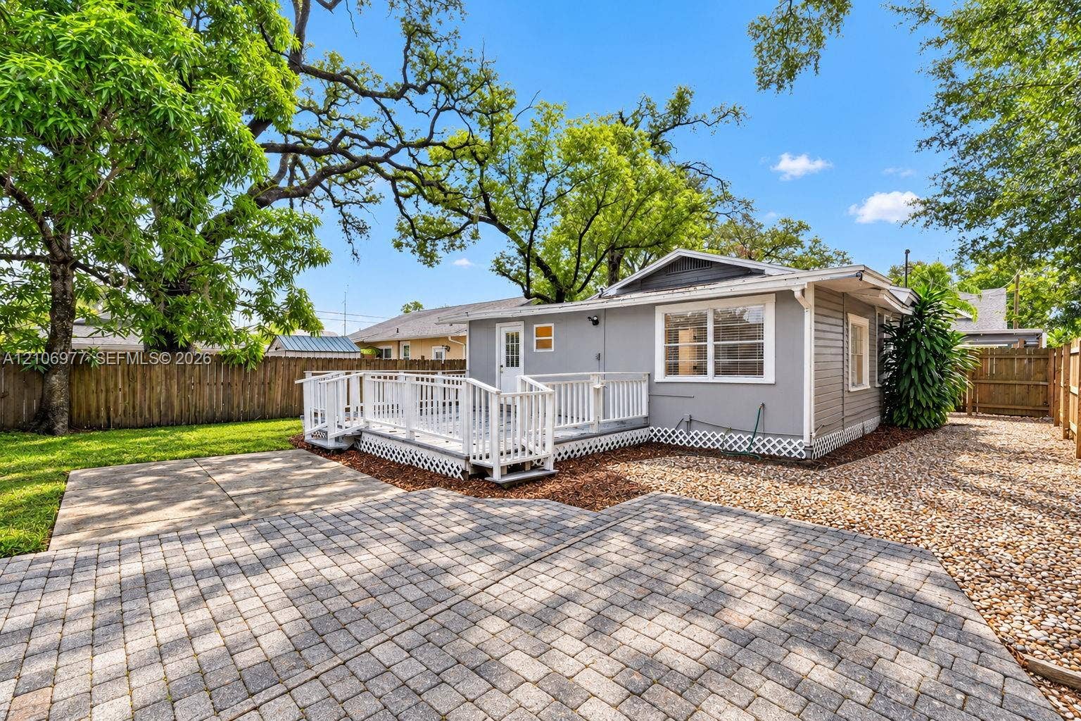 Exterior rear elevation featuring a raised white wooden deck, paver stone patio, gravel surfacing, and wood privacy fencing