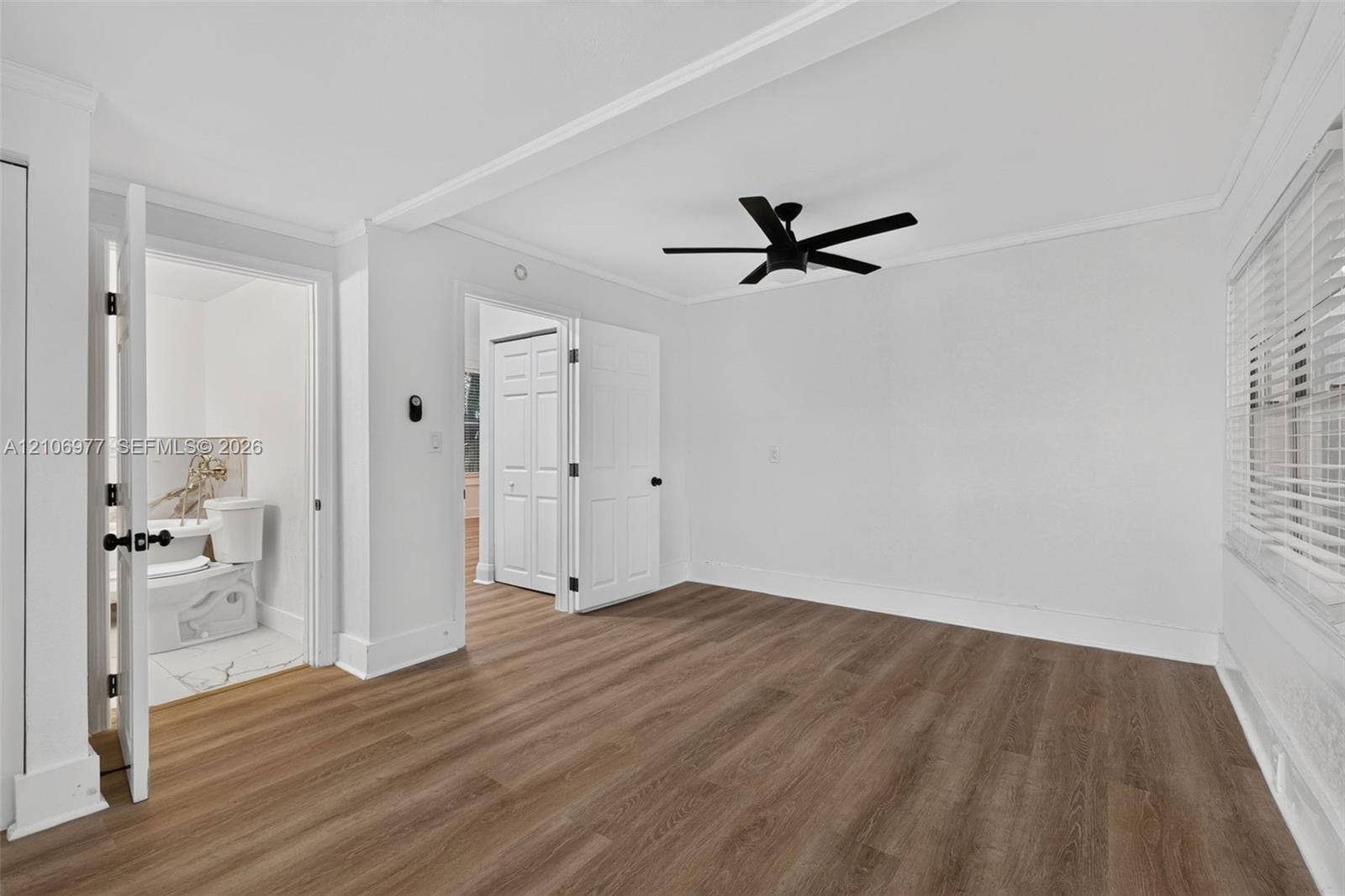Room featuring wood-finish flooring, a matte black ceiling fan, white interior doors, and horizontal slat window blinds