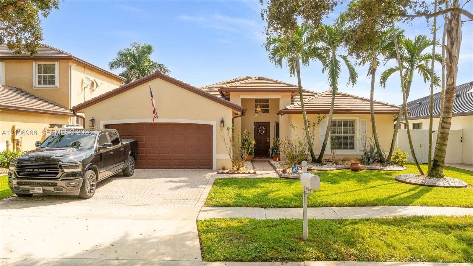 3801 SW 147th Avenue, Miramar, FL 33027 Stucco exterior residence featuring a paved driveway, a multi-car garage, tile roofing, and curated landscaping with mature palm trees