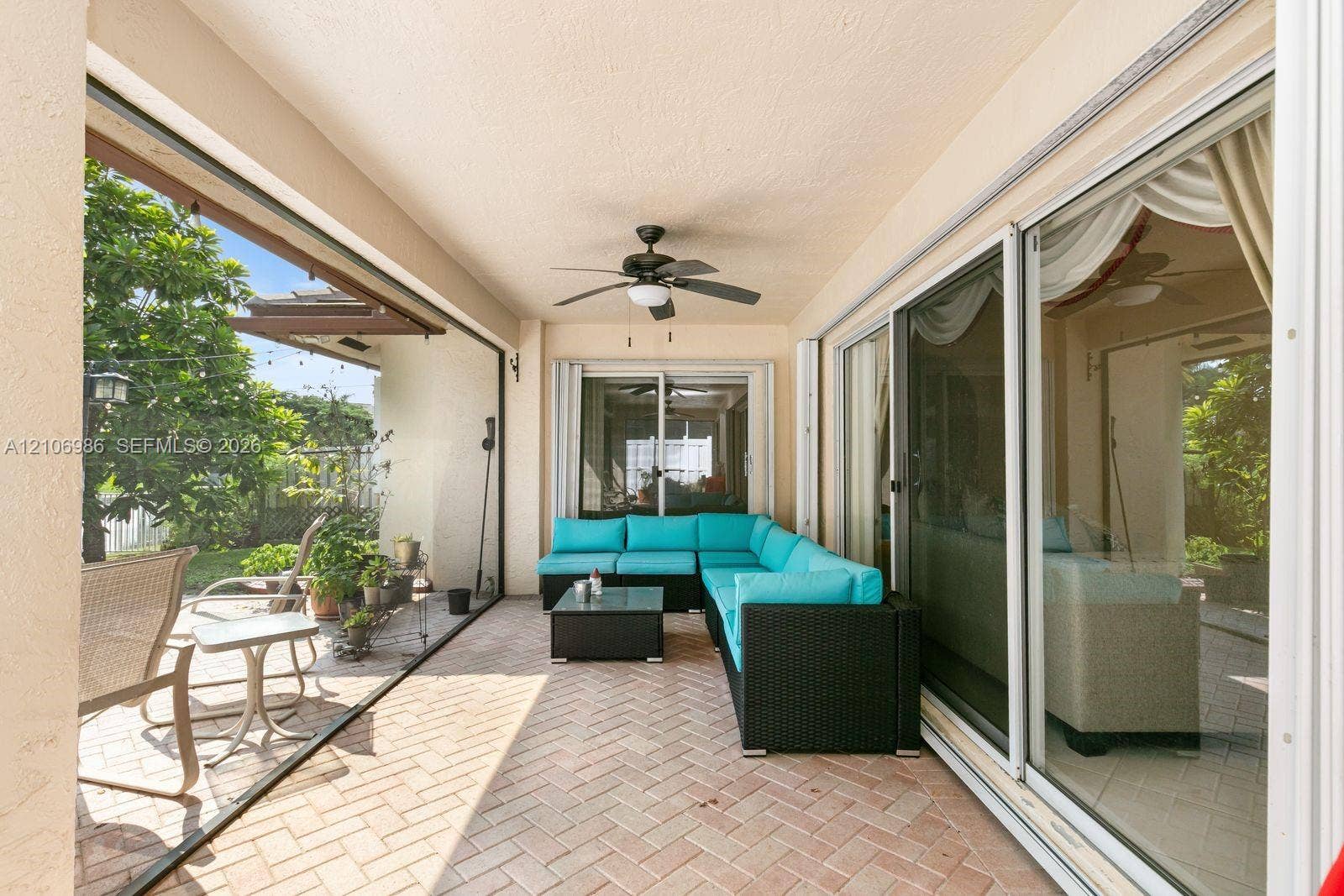3801 SW 147th Avenue, Miramar, FL 33027 Covered outdoor patio featuring herringbone-patterned brick pavers, large multi-panel sliding glass doors, and a ceiling-mounted fan