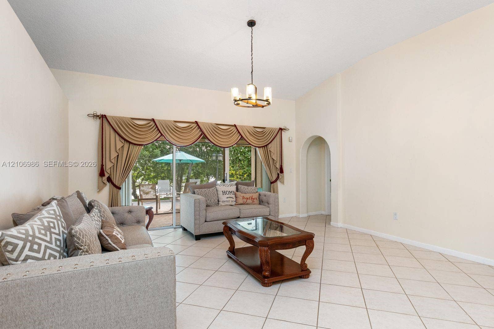 3801 SW 147th Avenue, Miramar, FL 33027 High-ceiling interior featuring light-colored ceramic tile flooring, a multi-arm candelabra-style chandelier, a recessed arched doorway, and a sliding glass door