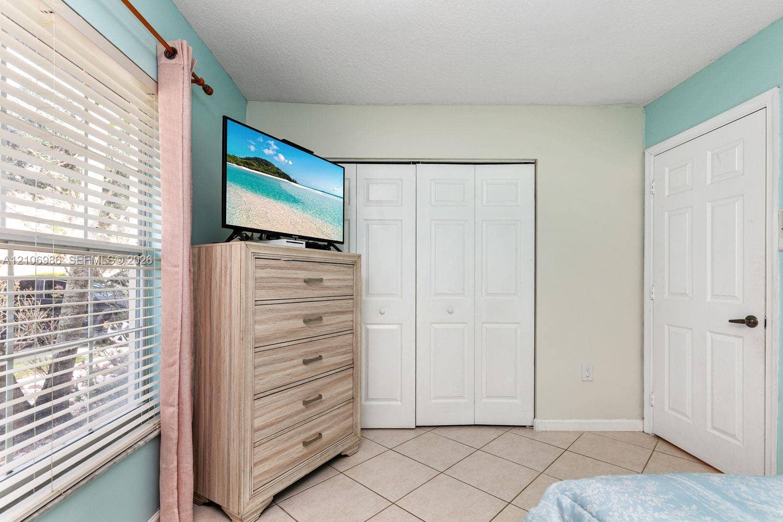 3801 SW 147th Avenue, Miramar, FL 33027 Ceramic tile flooring arranged in a diagonal pattern, white paneled bi-fold closet doors, a classic six-panel interior door, and a window with horizontal blinds