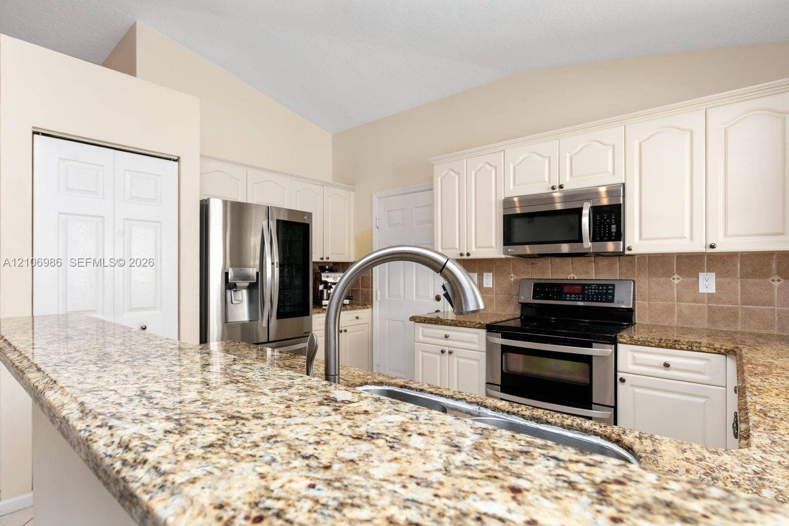 3801 SW 147th Avenue, Miramar, FL 33027 Kitchen featuring white cabinetry, stone countertops, a stainless steel refrigerator, a built-in microwave, and a high-arch gooseneck faucet