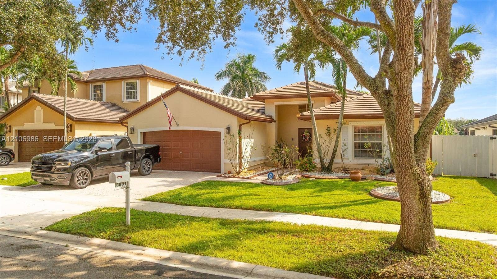 3801 SW 147th Avenue, Miramar, FL 33027 Stucco exterior residence featuring a multi-gable tile roof, attached two-car garage, and manicured front lawn with mature landscaping