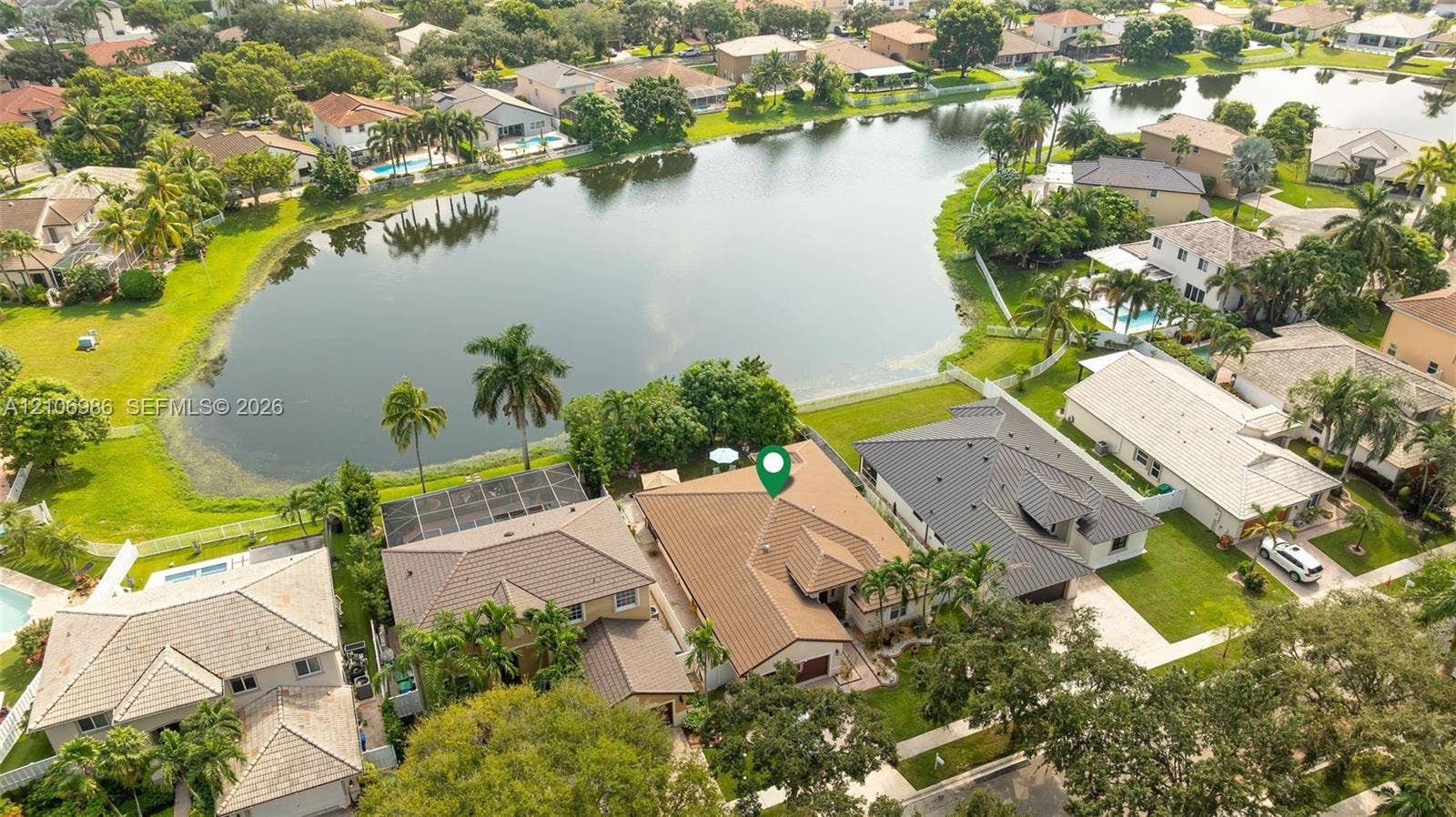 3801 SW 147th Avenue, Miramar, FL 33027 Aerial perspective of a multi-hip roofline property featuring a screened-in lanai, concrete tile roofing, and direct water frontage on a residential lake