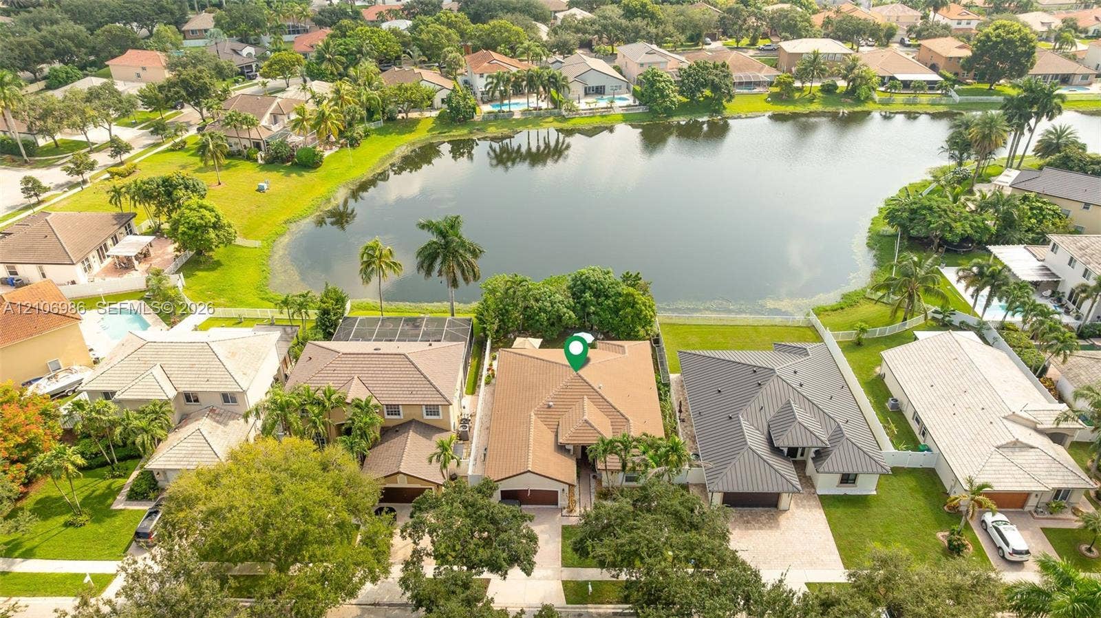 3801 SW 147th Avenue, Miramar, FL 33027 Aerial perspective of waterfront property featuring a multi-pitched shingle roof, paved driveway, attached garage, and landscaped grounds