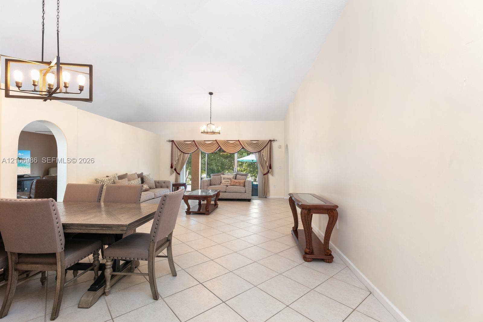 3801 SW 147th Avenue, Miramar, FL 33027 Open-concept living space featuring high ceilings, diagonal tile flooring, dual geometric chandeliers, and a large arched entryway