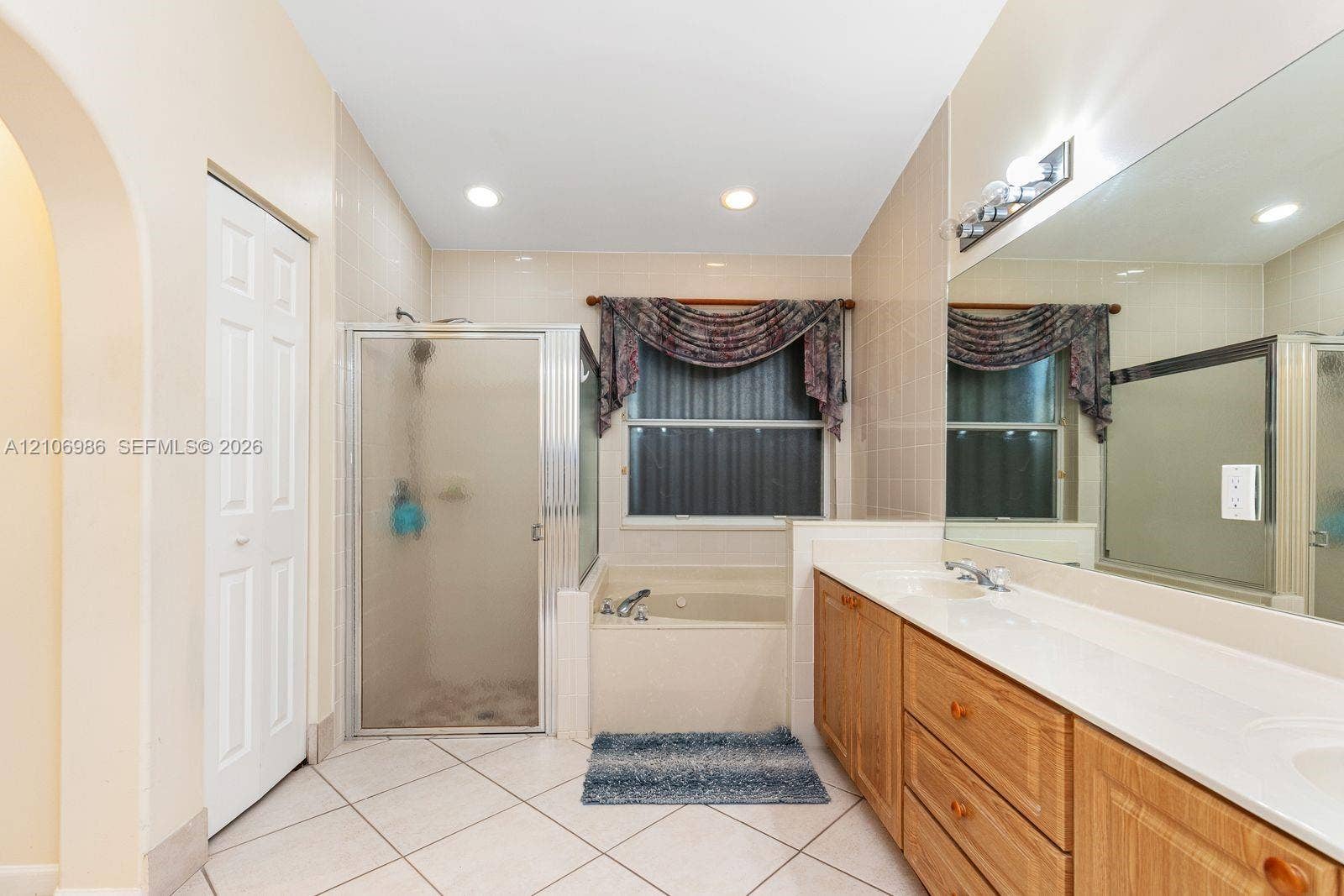3801 SW 147th Avenue, Miramar, FL 33027 Bathroom featuring a dual-sink vanity with light wood-finish cabinetry, a tiled soaking tub, a separate glass-enclosed shower, and a large wall-mounted mirror