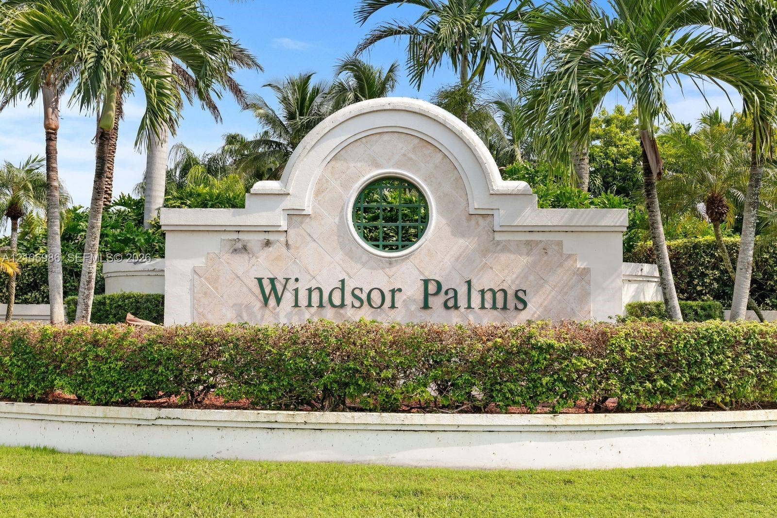 3801 SW 147th Avenue, Miramar, FL 33027 Masonry entrance monument featuring a central circular window, decorative stone-textured paneling, and a manicured perimeter of mature palm trees and sculpted shrubbery