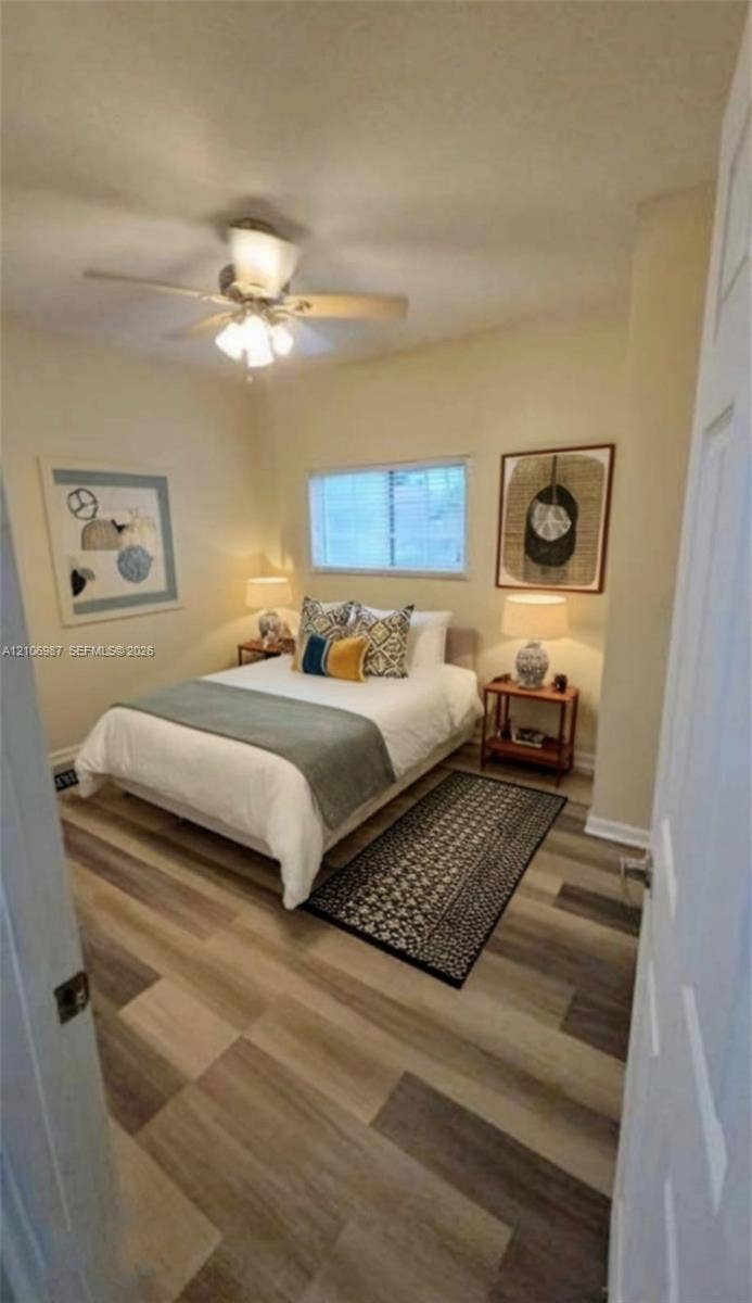 Room featuring wood-finish flooring, a central ceiling fan with integrated lighting, and a window with blinds