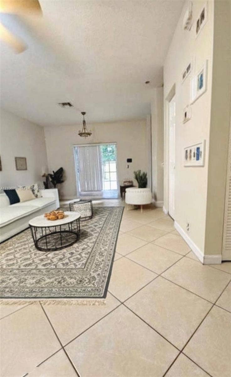 Open-concept interior featuring large-format diagonal tile flooring, high ceilings, sliding glass patio doors, and a decorative chandelier