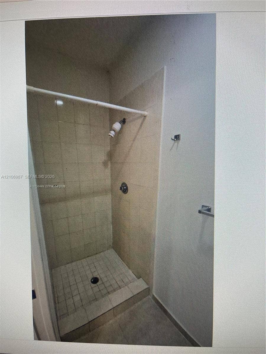 Walk-in shower featuring light-toned tile wall surround, grid-pattern floor tiling, and a metal shower head