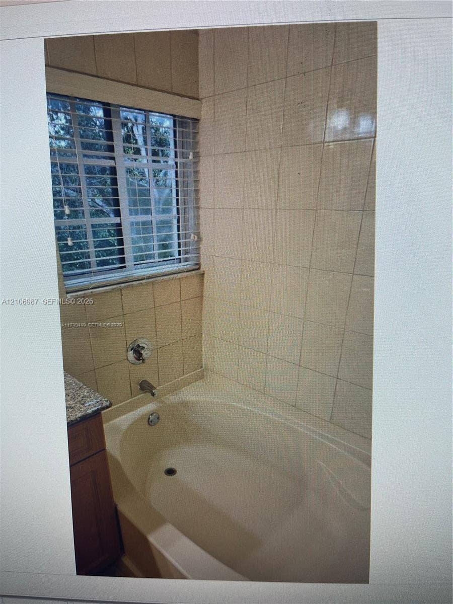 Deep soaking bathtub featuring tiled walls, integrated faucet hardware, and a window with horizontal blinds
