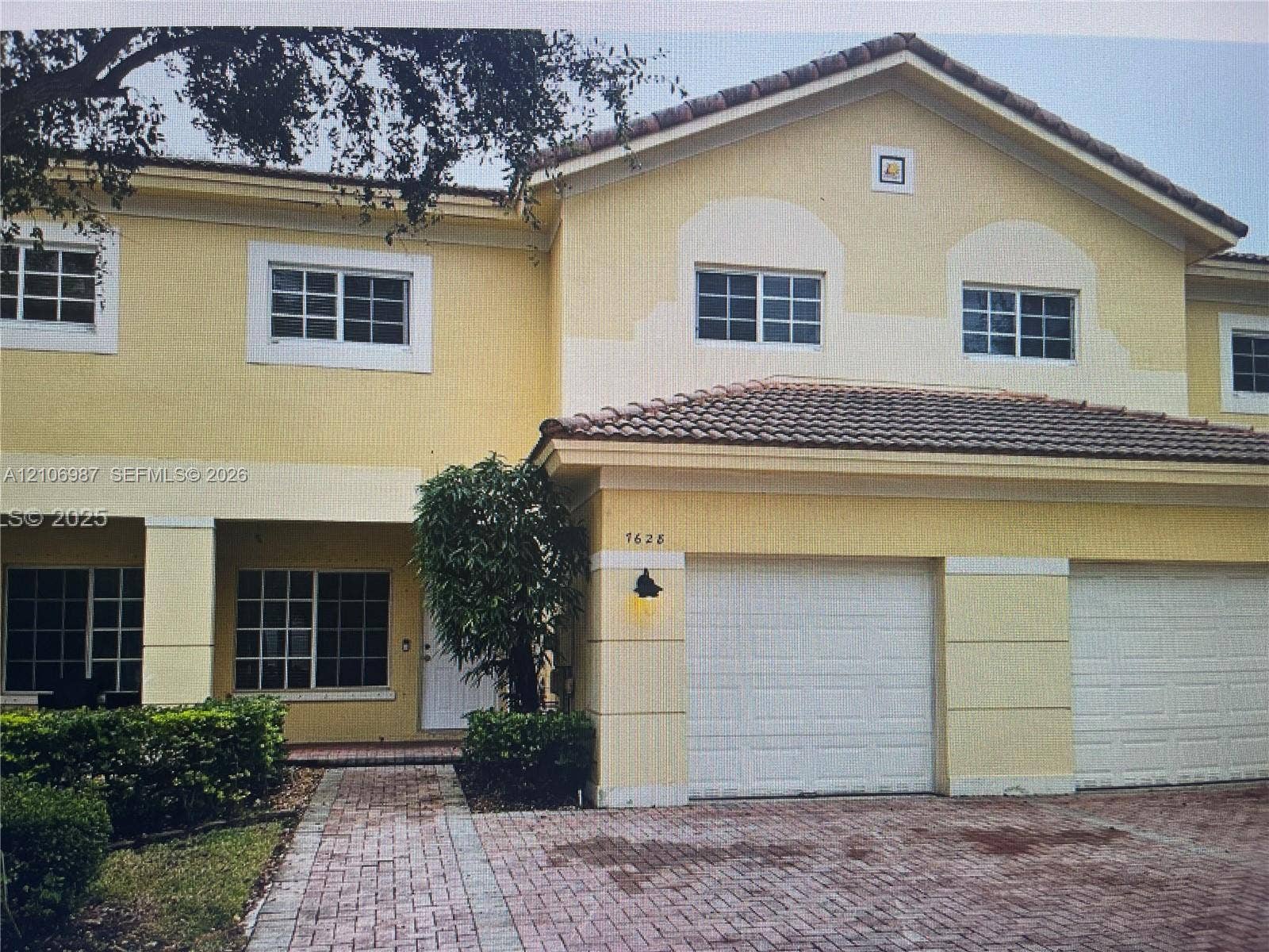 Stucco exterior featuring a dual-car garage, pitched tile roofing, multi-pane windows, and a brick-paver driveway
