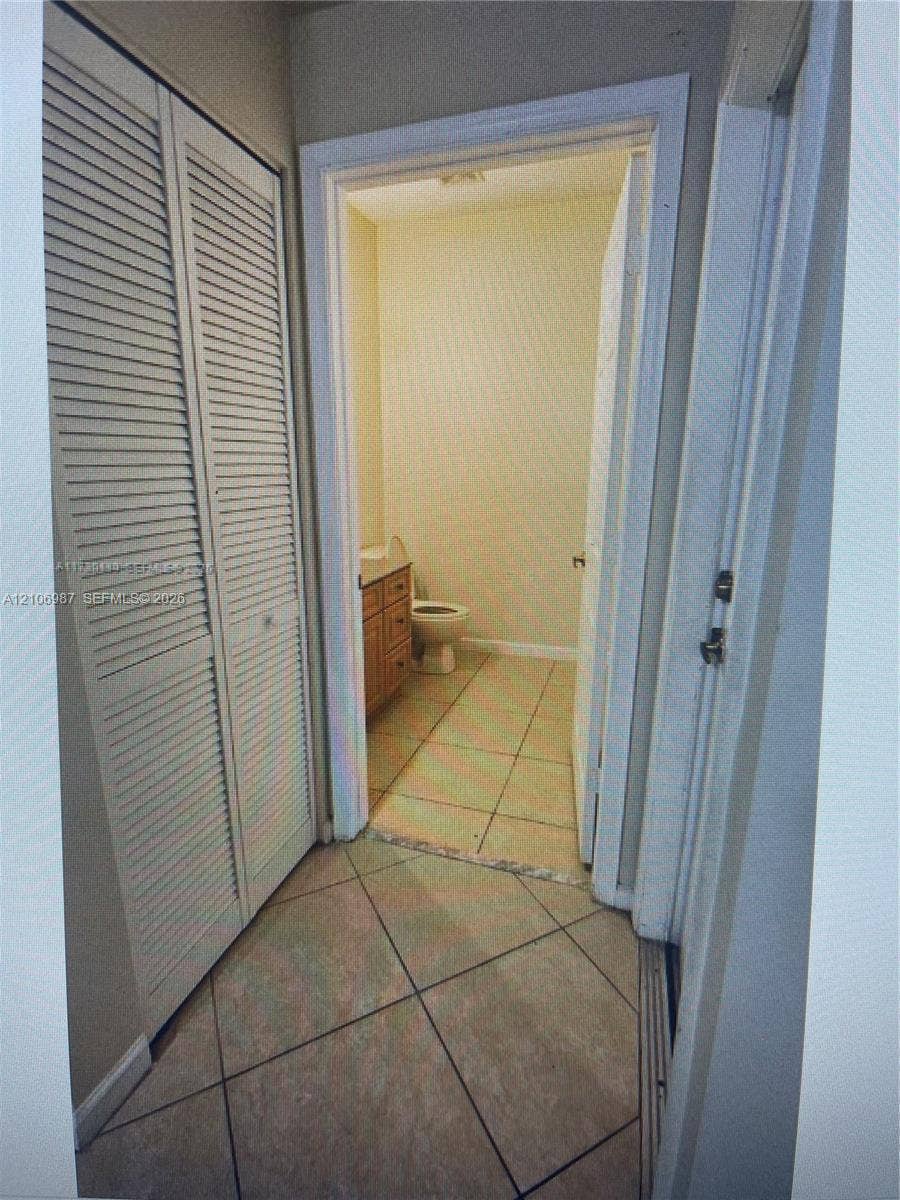 Louvered bi-fold closet doors, neutral ceramic floor tiling, and a wooden vanity cabinet