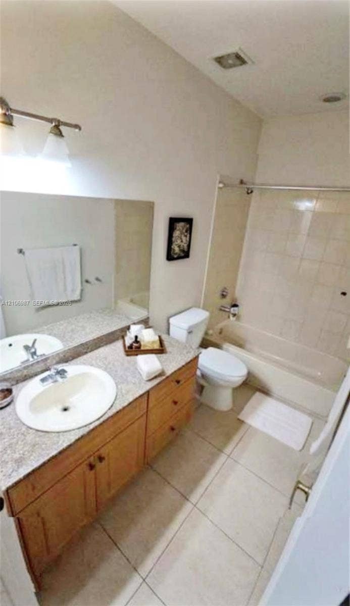Bathroom featuring a vanity with a stone-finish countertop, oval undermount sink, three-light fixture, and light-tone tile flooring