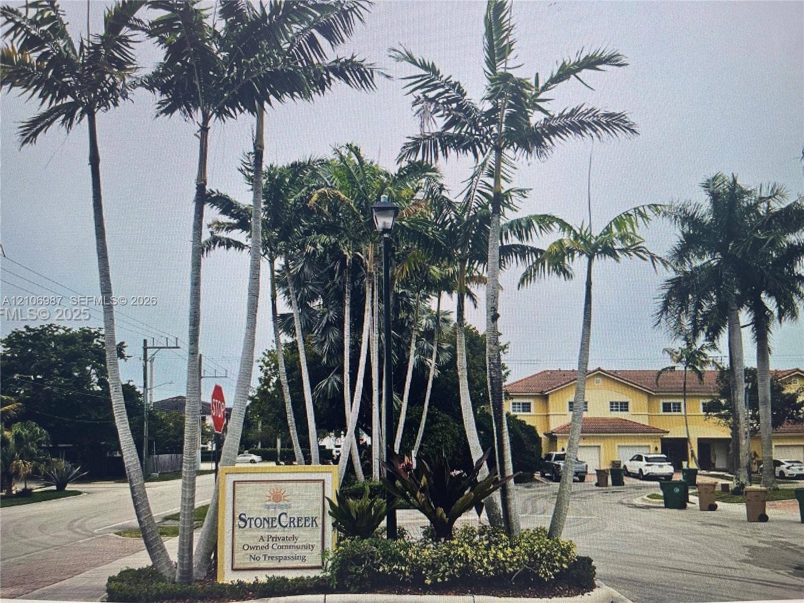 Stone Creek community entrance featuring mature palm trees, professional landscaping, a monument sign, and asphalt paving