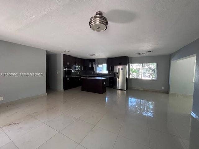 Kitchen featuring dark cabinetry, center island, stone-finish countertops, stainless steel appliances, and large-format tile flooring