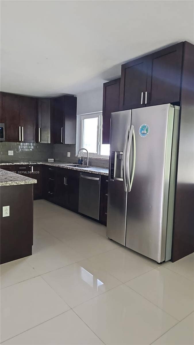 Kitchen featuring dark wood-finish cabinetry, stone-surface countertops, stainless steel appliances, and tile flooring
