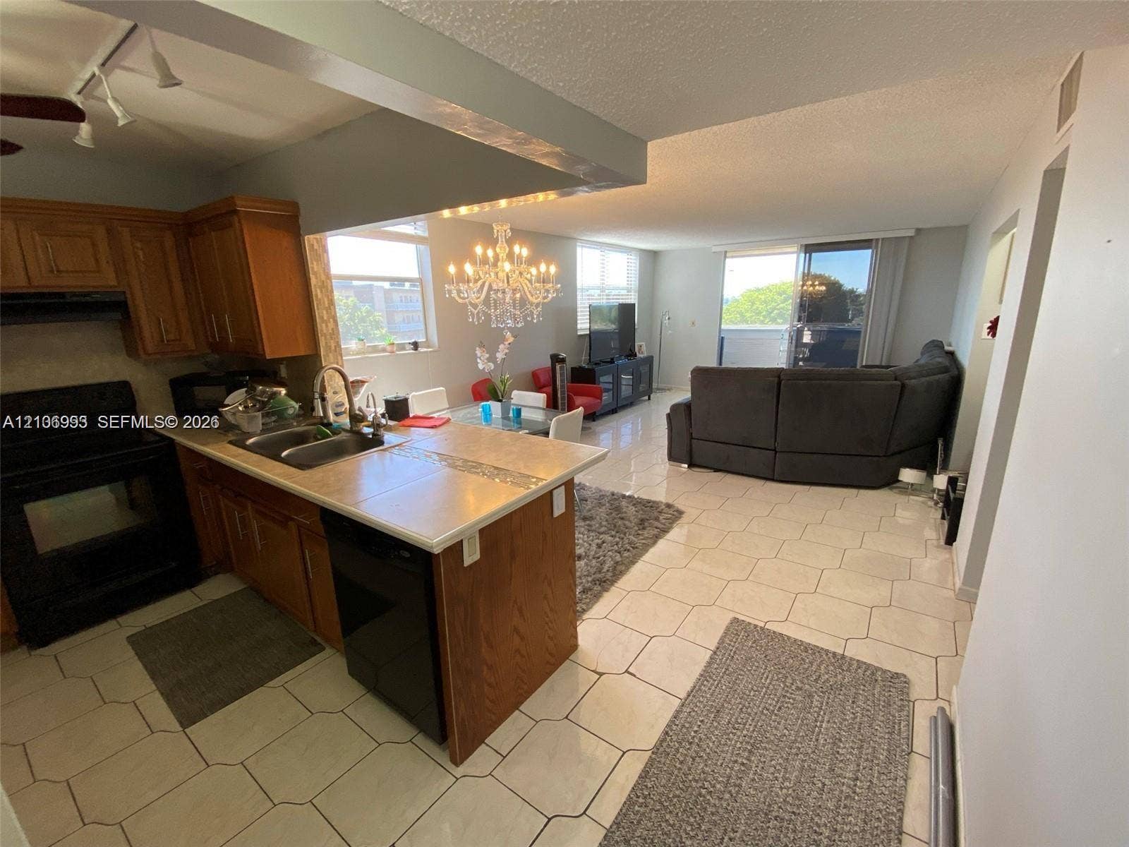 410 NW 68th Avenue, #515, Plantation, Plantation, FL 33317 Kitchen featuring wood cabinetry, tile countertops, stainless steel dual-basin sink, and track lighting, complemented by tile flooring and an ornate chandelier