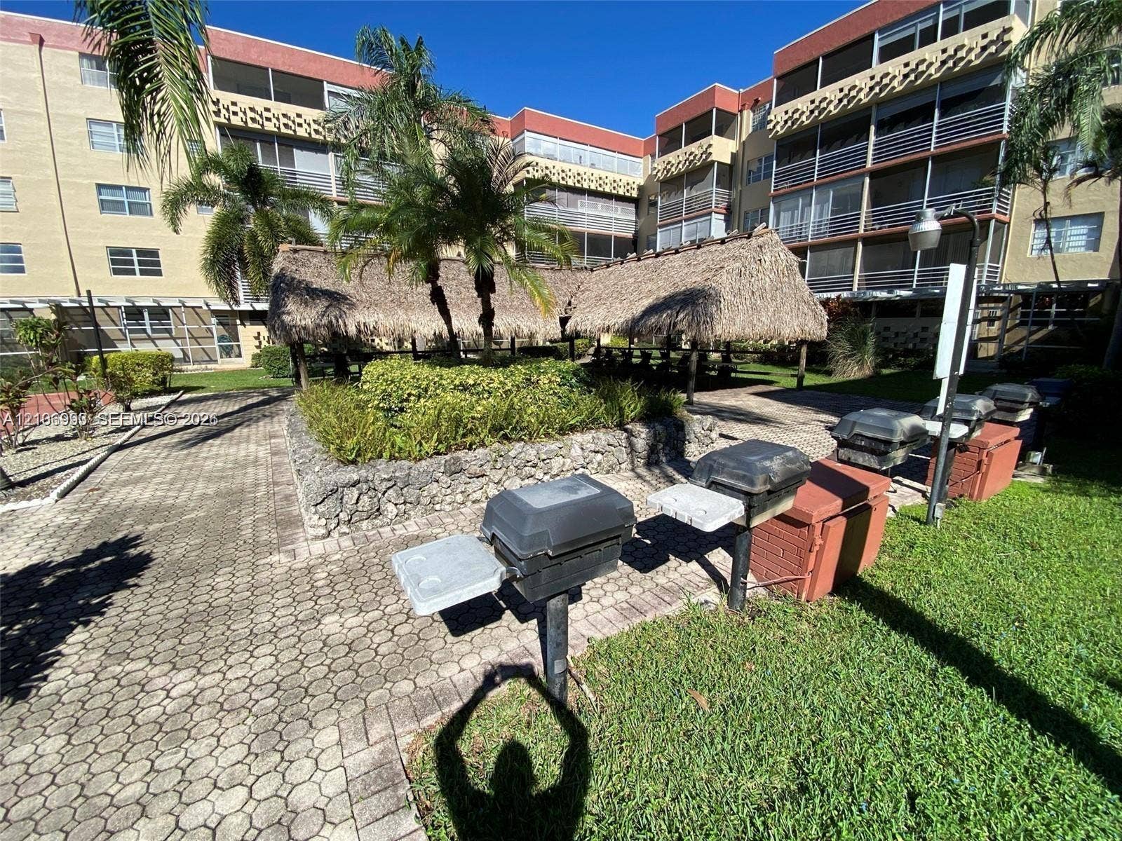 410 NW 68th Avenue, #515, Plantation, Plantation, FL 33317 Common area featuring a paved brick patio, thatched-roof tiki hut, stone-lined landscaping, built-in charcoal grills, and mature palm trees