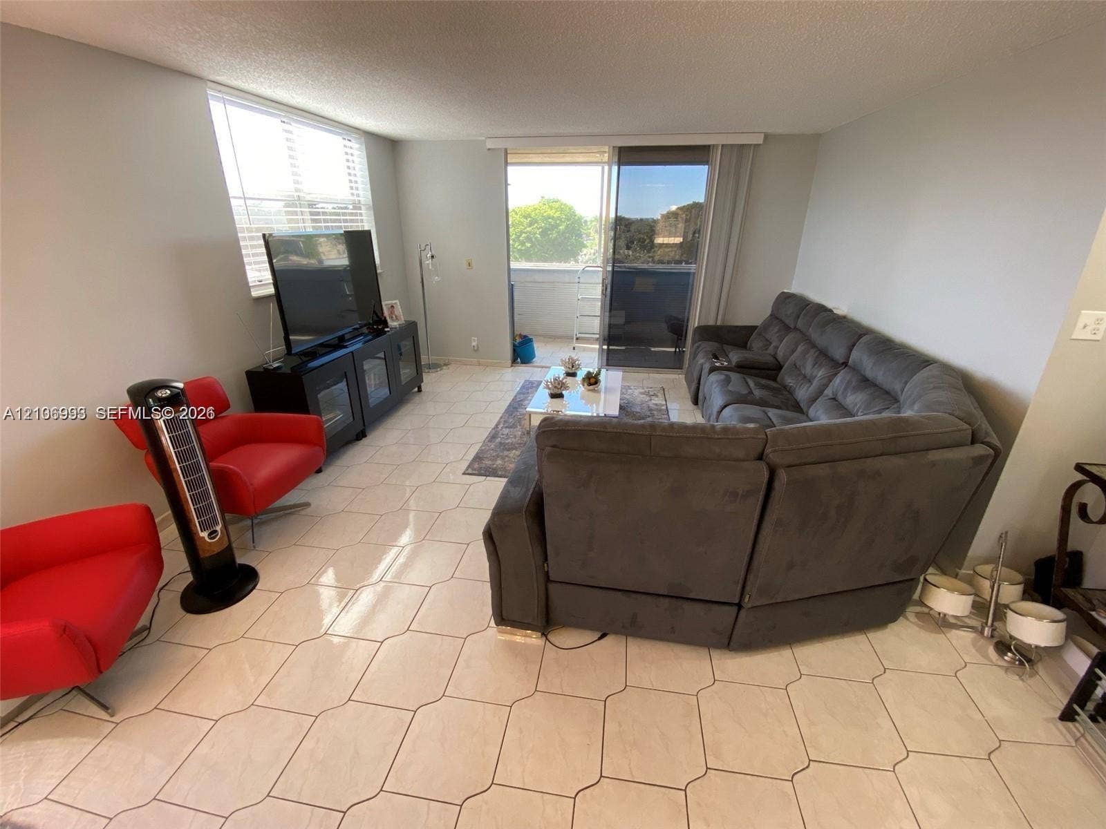 410 NW 68th Avenue, #515, Plantation, Plantation, FL 33317 Neutral-toned living space featuring light-colored tile flooring, window blinds, and sliding glass doors with access to an exterior balcony